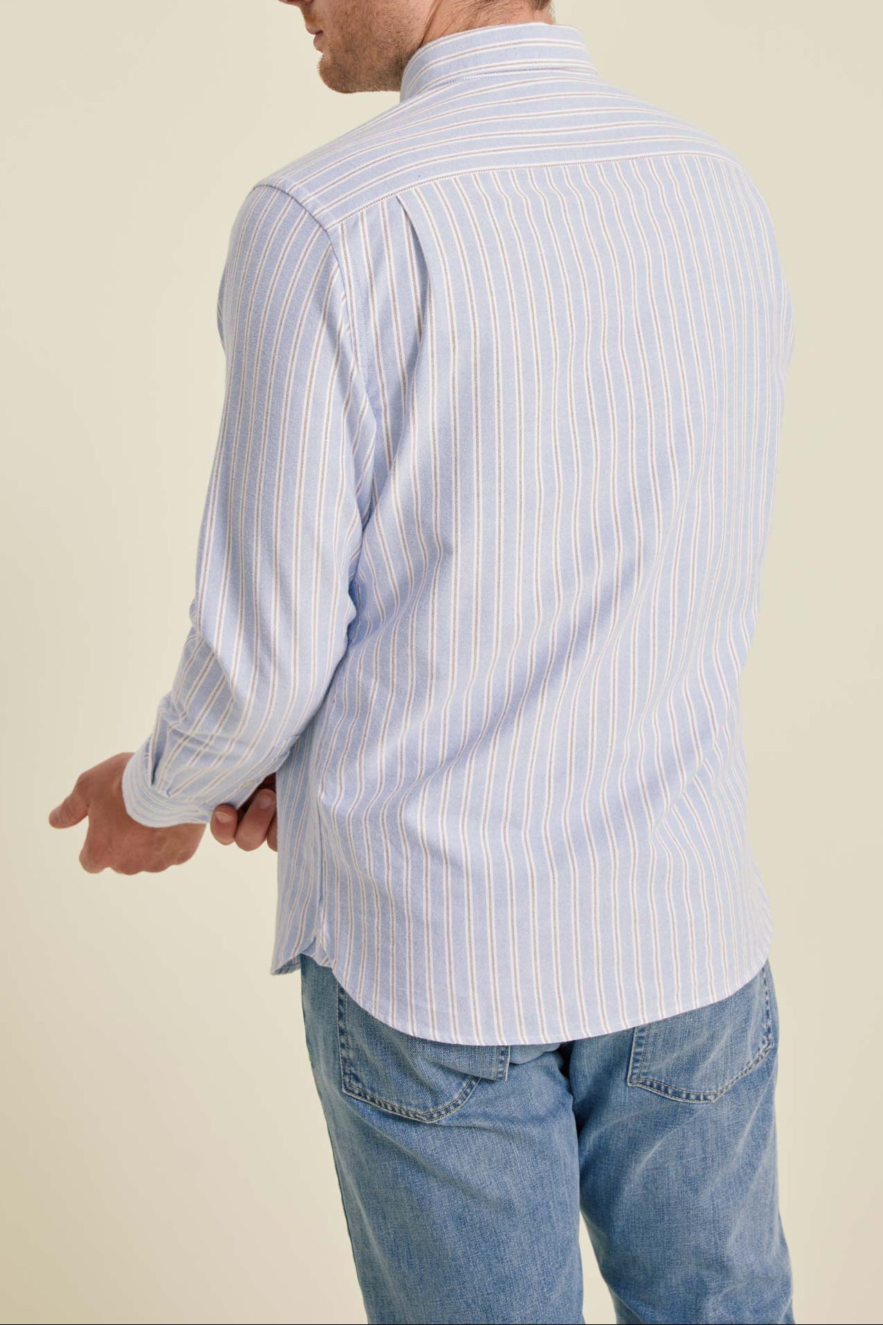 Man wearing a light blue striped shirt and jeans on a beige background