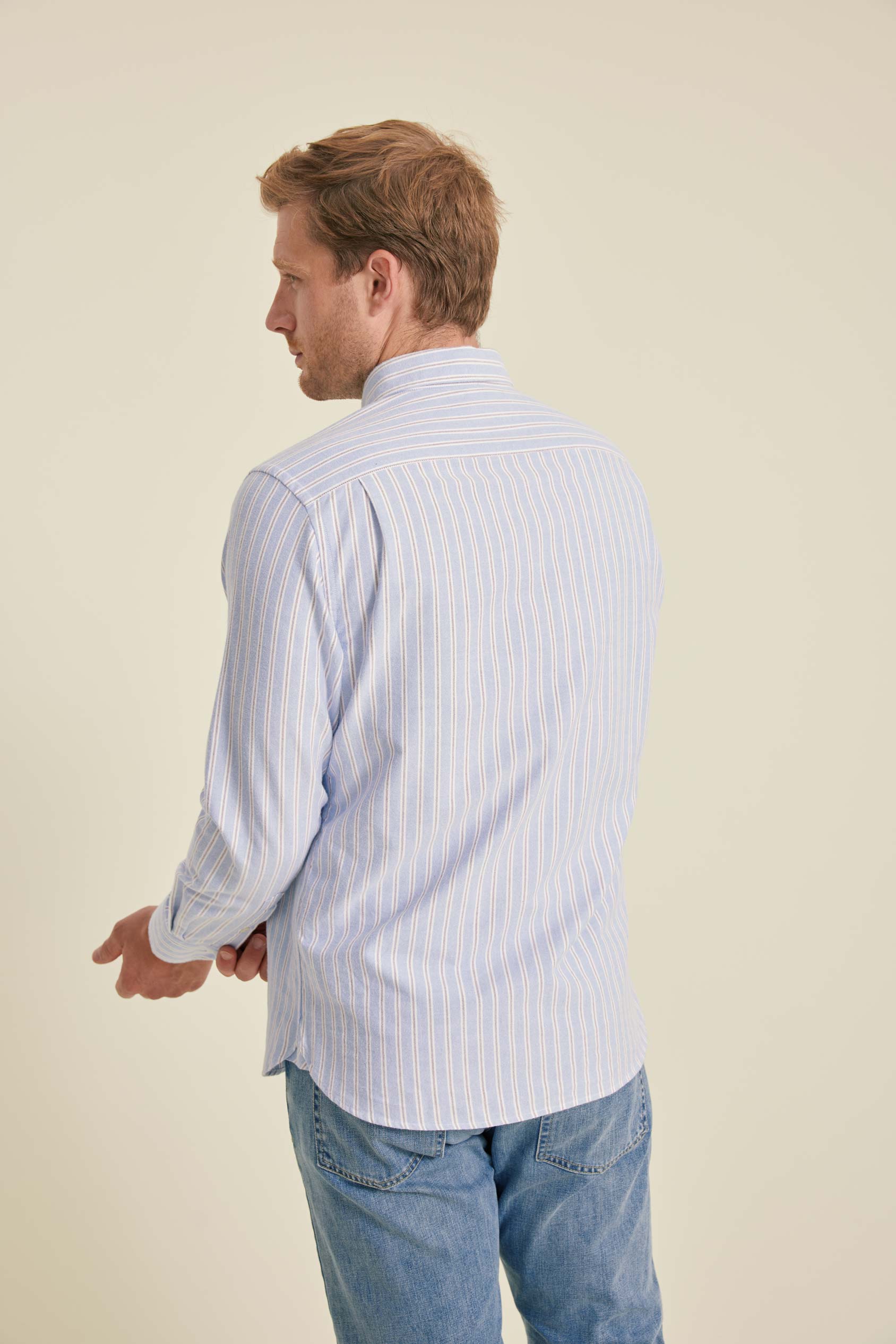 Man wearing a light blue striped shirt and jeans on a beige background