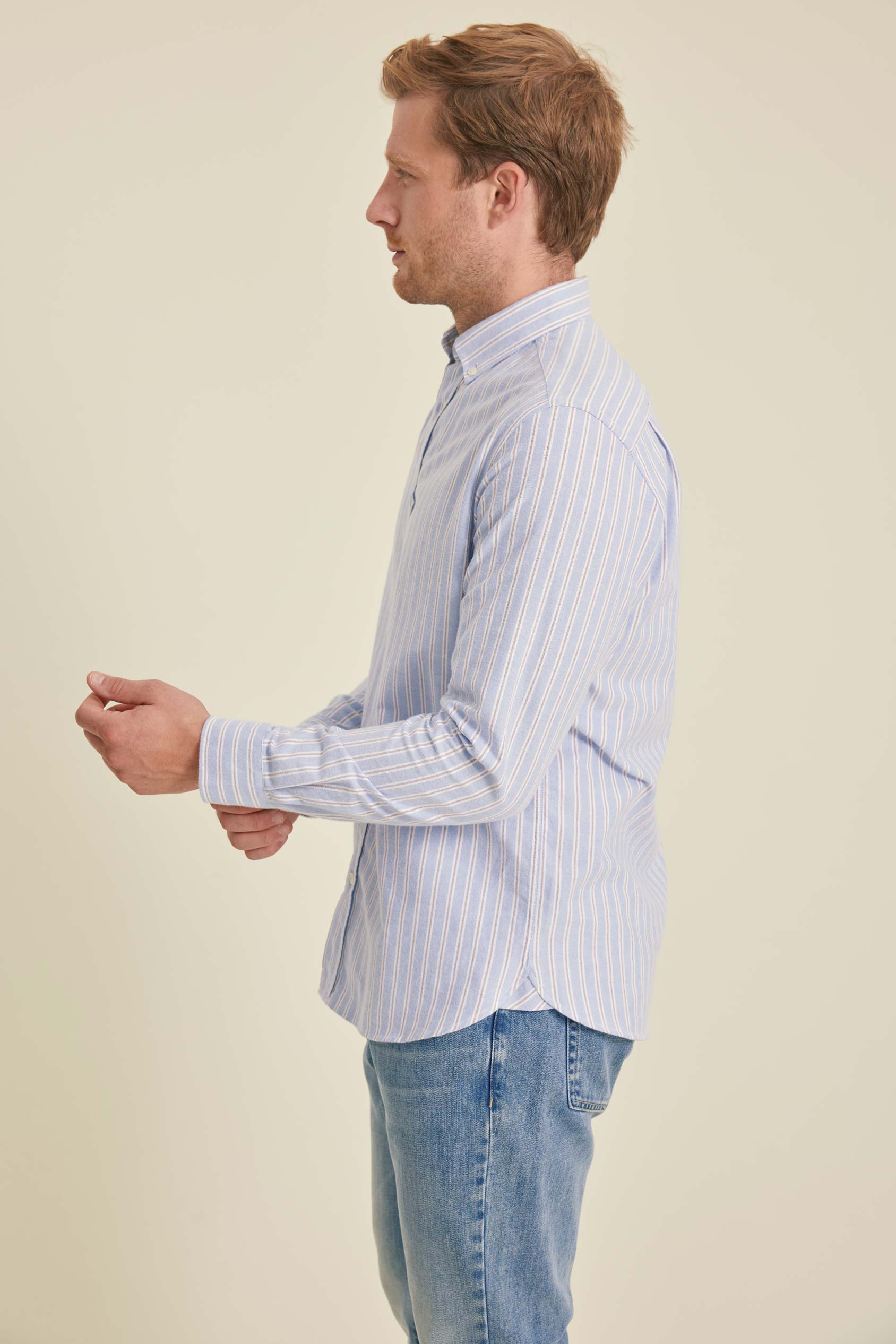 Man wearing a light blue striped shirt and jeans against a beige background