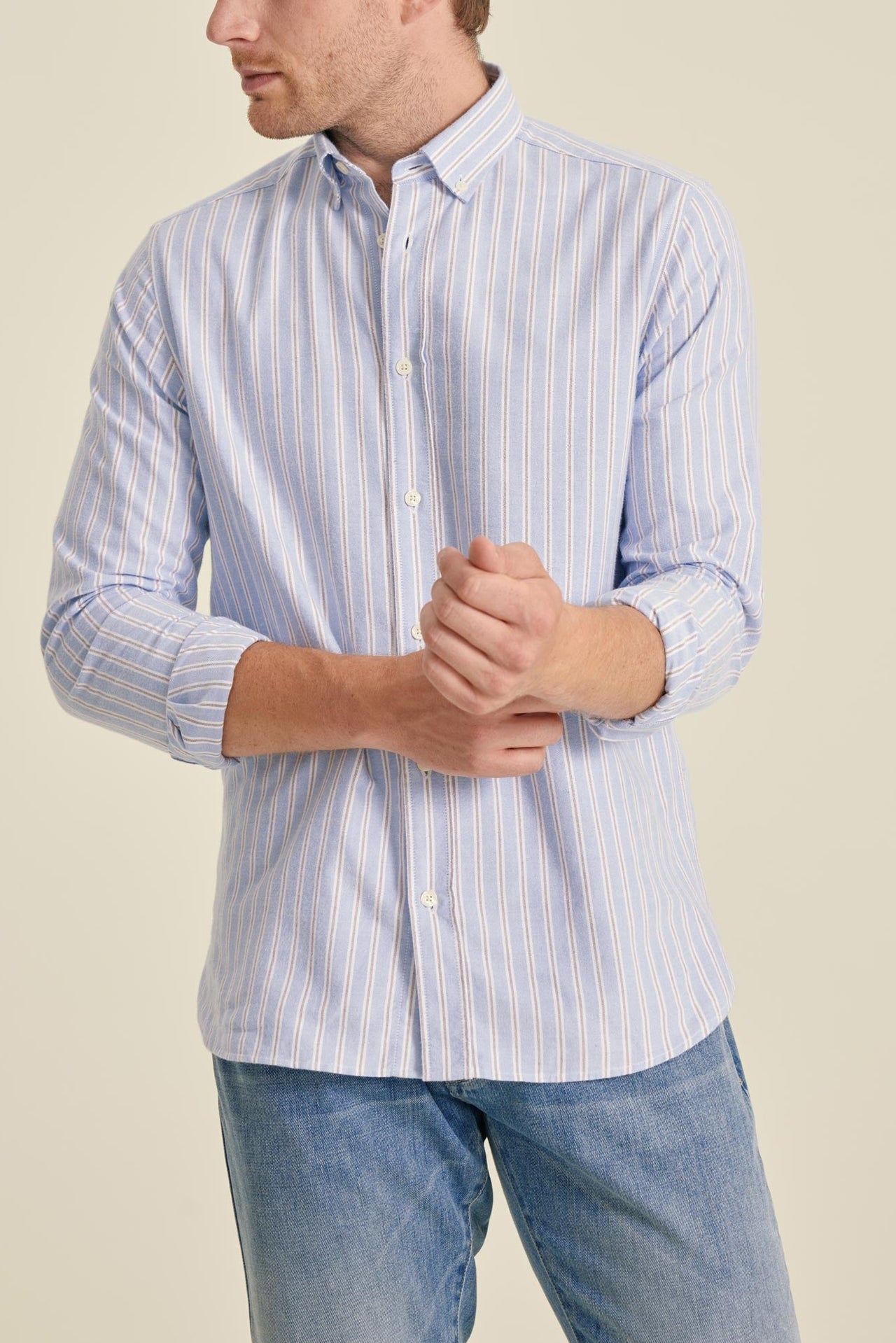 Man wearing a light blue striped shirt and jeans on a beige background
