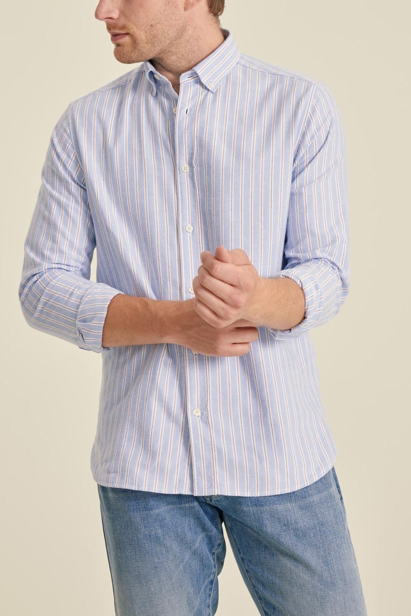 Man wearing a light blue striped shirt and jeans on a beige background