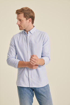 Man wearing a light blue striped shirt and jeans on a beige background