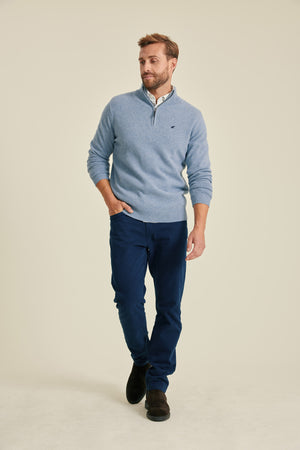 Man wearing a blue sweater and navy pants on a beige background