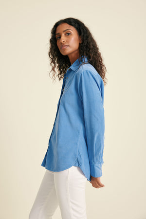 Woman wearing a light blue shirt and white pants on a beige background