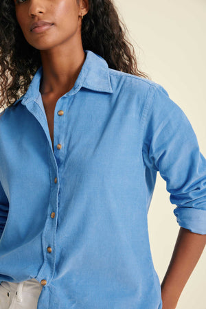Woman wearing a blue button-up shirt against a beige background