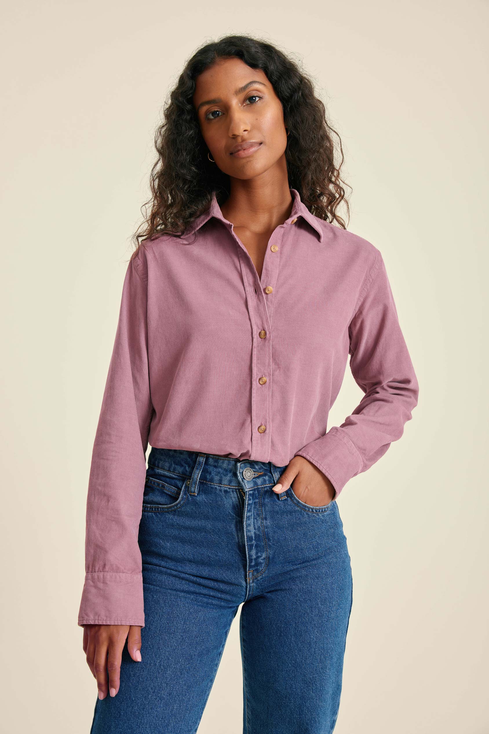 Woman wearing a pink shirt and blue jeans against a beige background