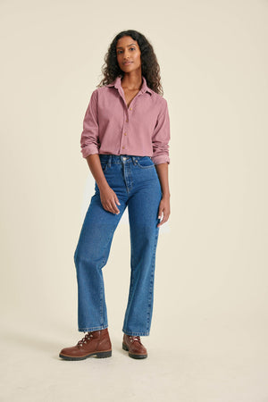 Woman wearing a pink shirt, blue jeans, and brown boots on a beige background