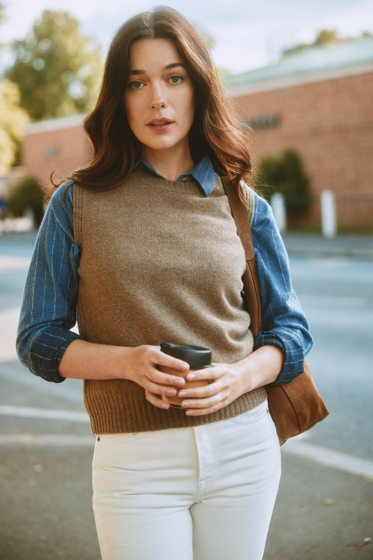 Woman holding a coffee cup and a bag, standing outdoors.