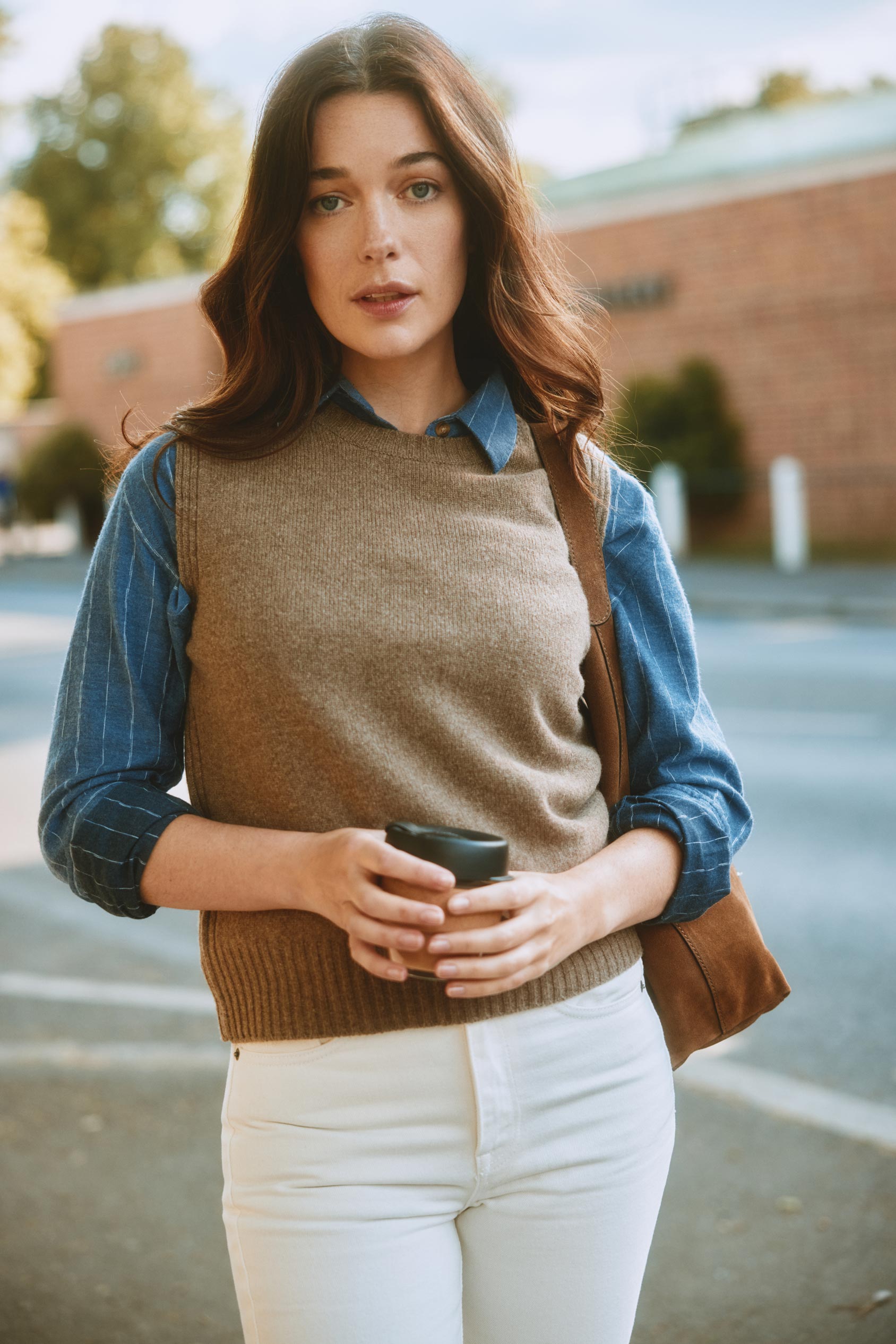 Woman holding a coffee cup and a bag, standing outdoors.