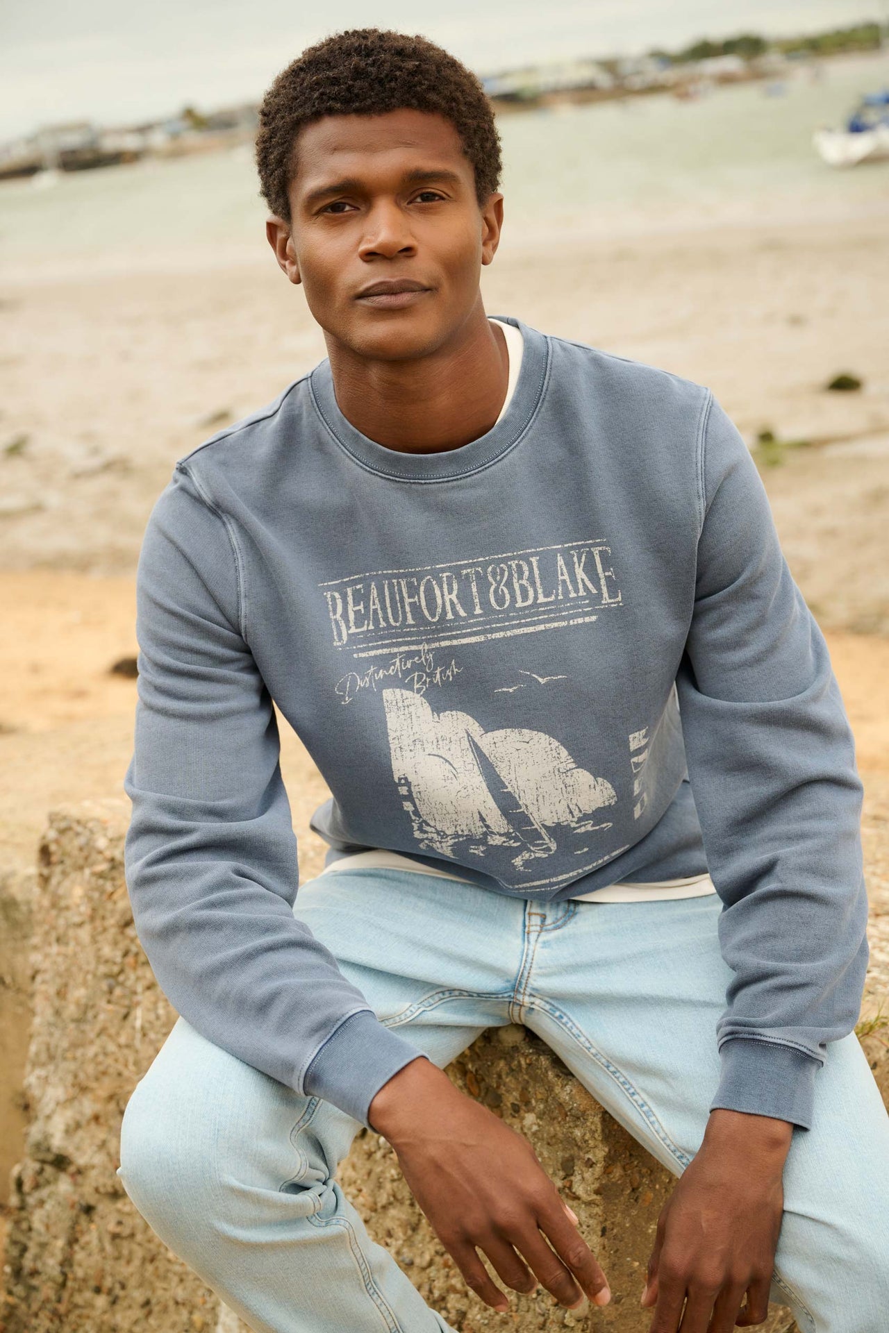 Man wearing a blue sweatshirt with 'Beaufort & Blake' branding on a beach.