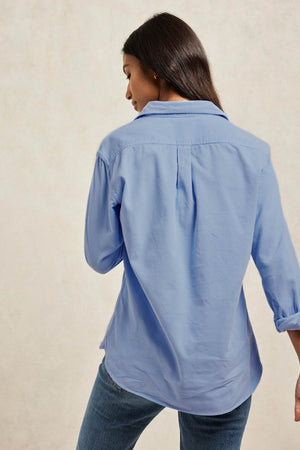 Fine needle cord women’s cornflower blue shirt with a back box pleat and curved hem for ease. 100% Cotton. Cut from soft needlecord to a classic fit with vintage buttons. Casual wear. Size XS, S, M, L, XL. Made in Portugal. Machine wash. Boyfriend fit.