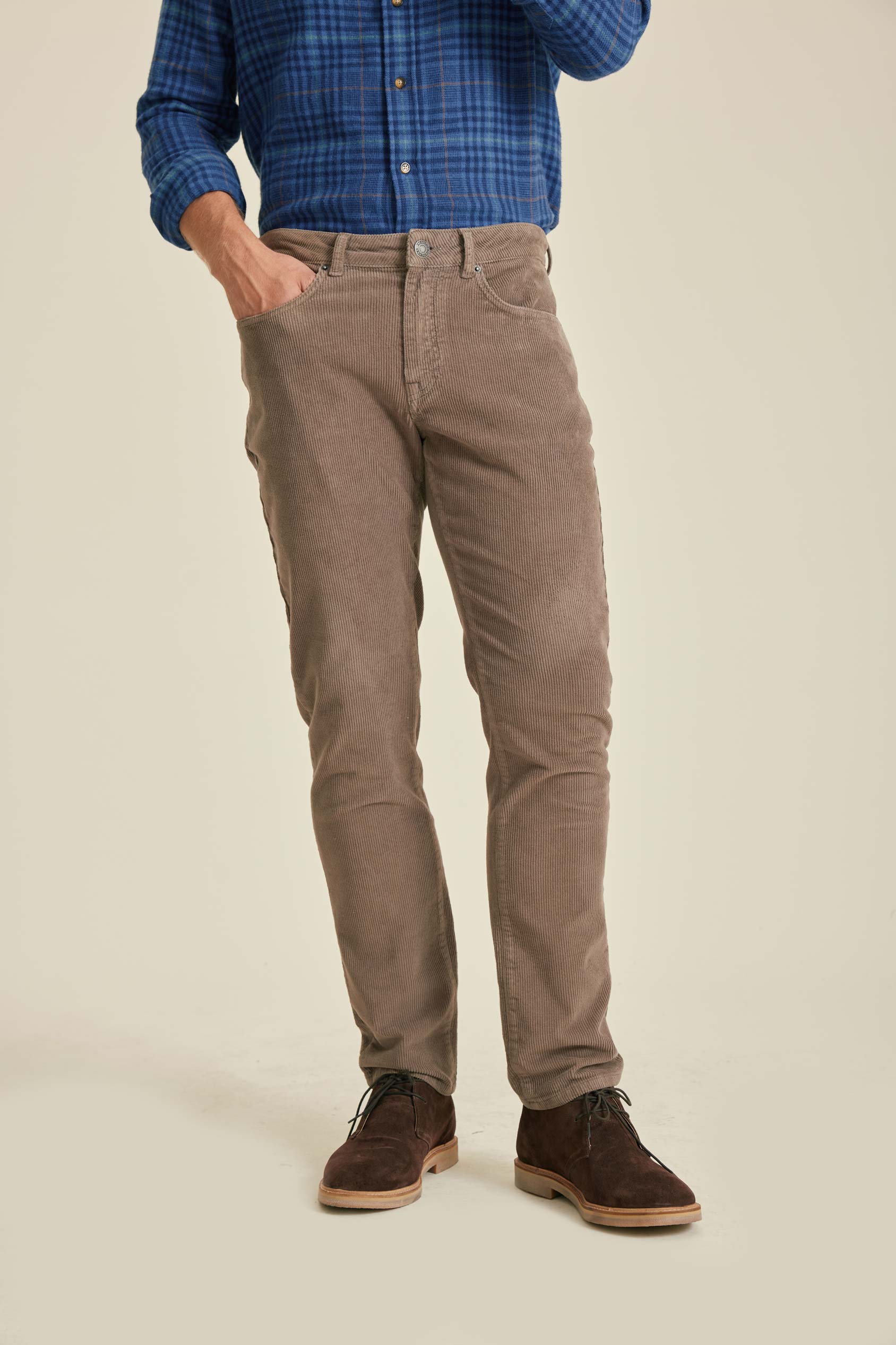 Person wearing brown pants and a blue plaid shirt on a beige background