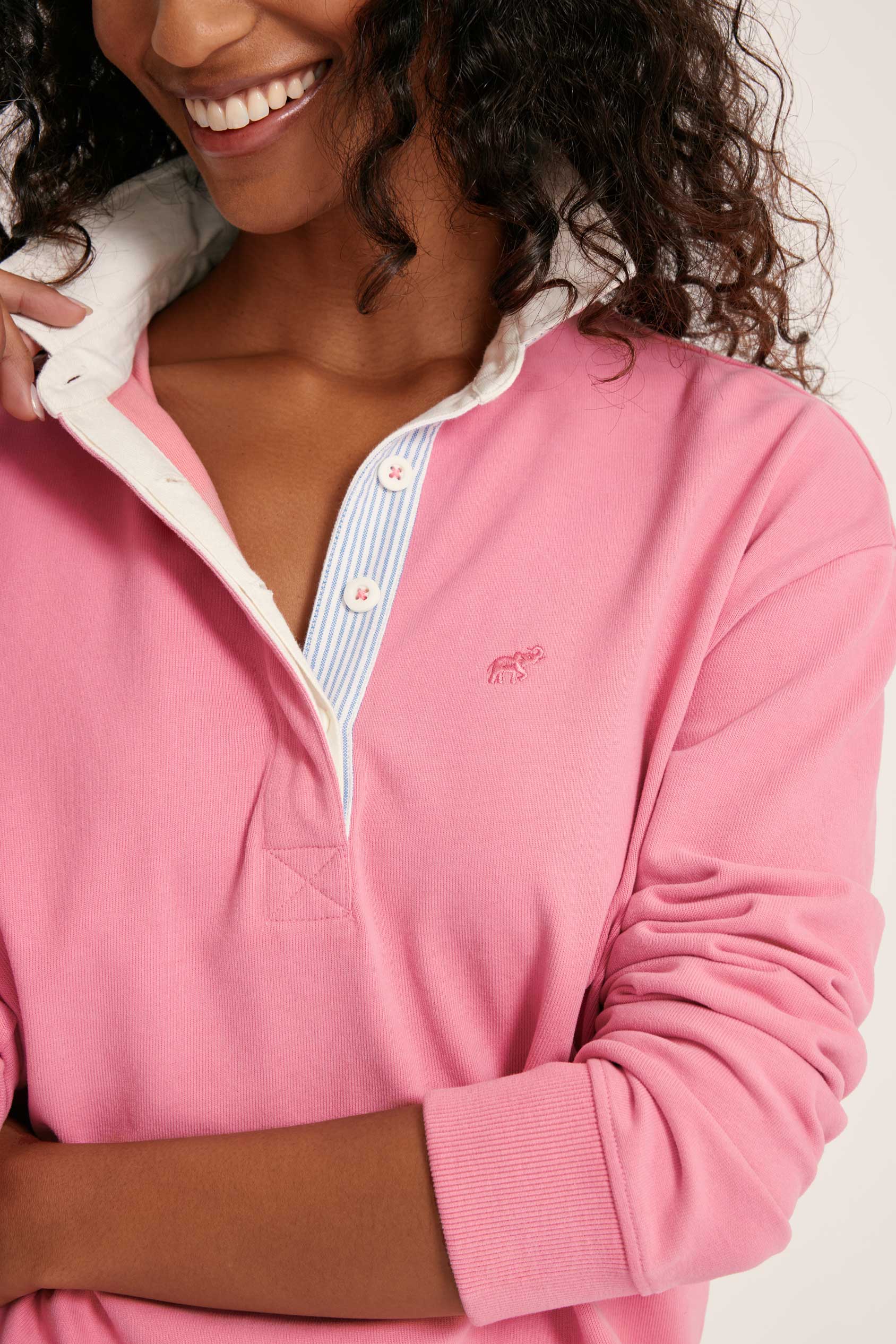 Person wearing a pink long-sleeve shirt with a collar, smiling.