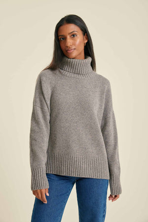 Woman wearing a gray turtleneck sweater and blue jeans on a beige background