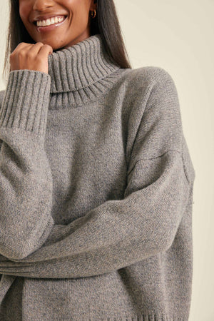 Person wearing a gray turtleneck sweater against a neutral background