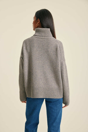 Person wearing a gray sweater and blue jeans on a beige background