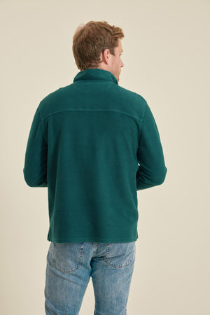Man wearing a green fleece jacket and blue jeans on a beige background