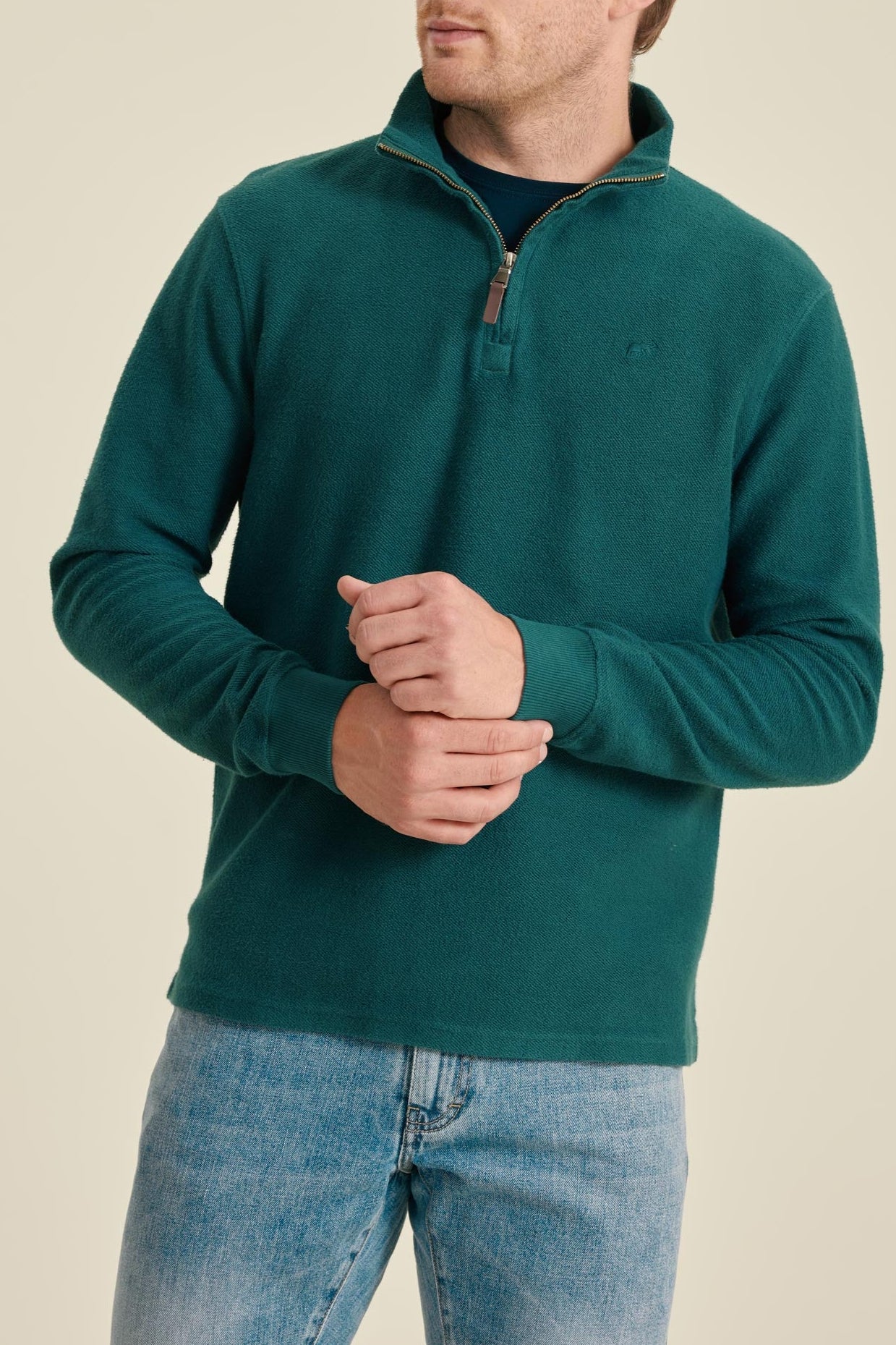 Man wearing a teal fleece pullover and jeans on a beige background