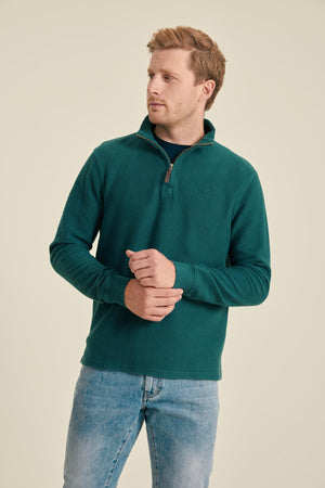 Man wearing a teal fleece pullover and jeans on a beige background