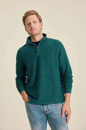 Man wearing a teal fleece pullover and jeans on a beige background