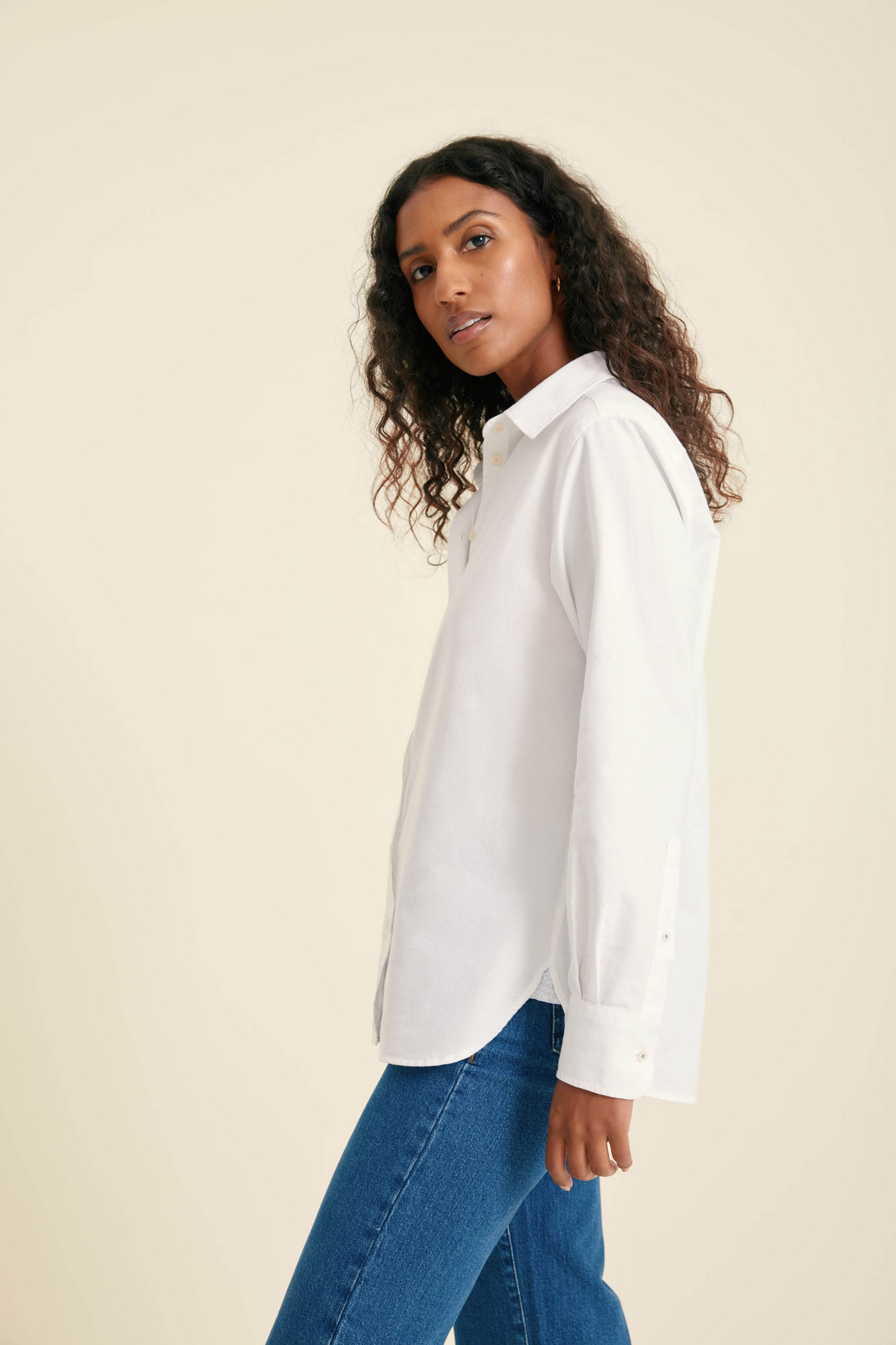 Woman wearing a white shirt and blue jeans against a beige background