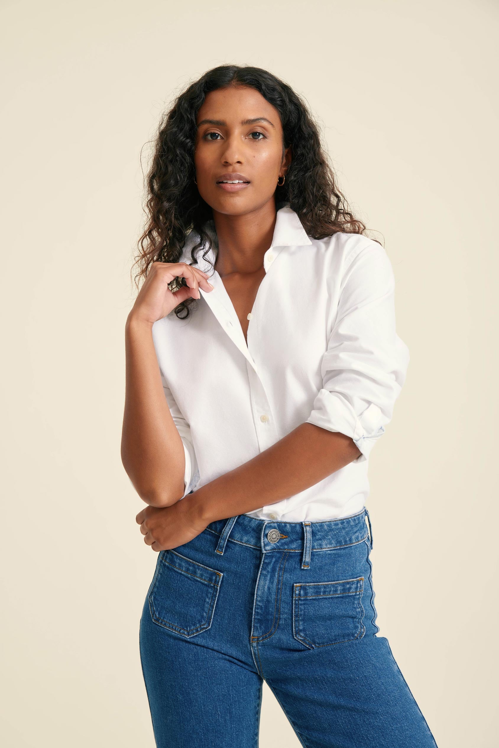 Woman wearing a white shirt and blue jeans against a beige background