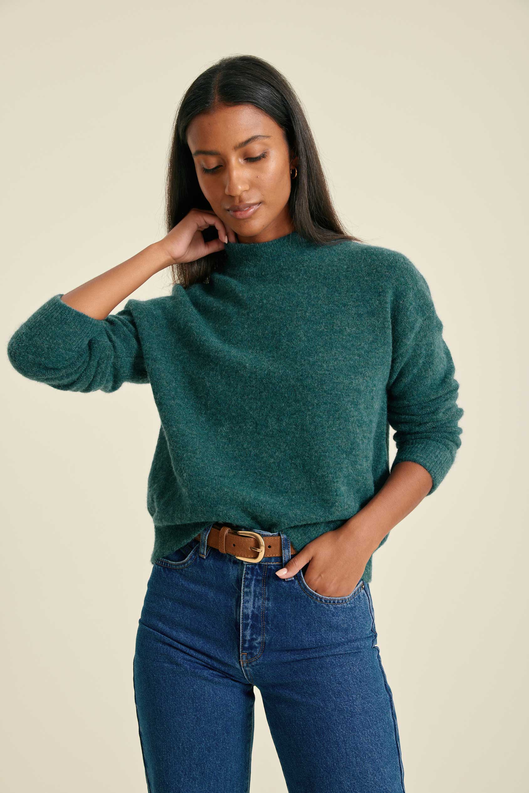 Woman wearing a teal sweater and blue jeans against a beige background