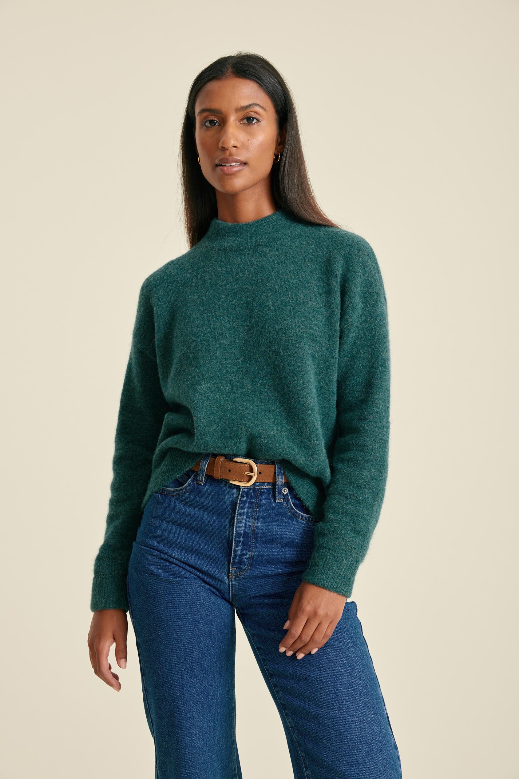 Woman wearing a green sweater and blue jeans on a beige background