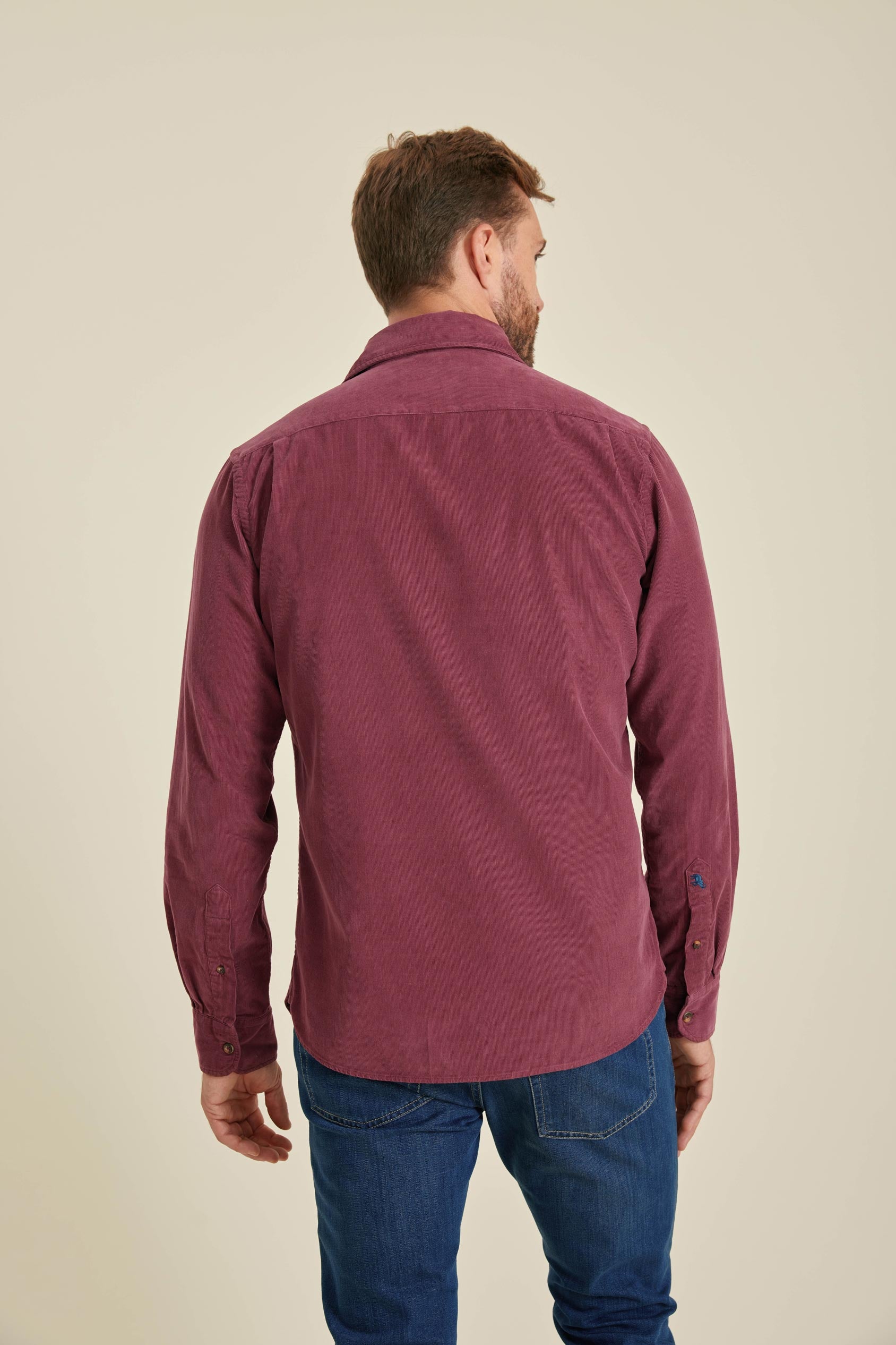 Man wearing a burgundy shirt and blue jeans on a beige background