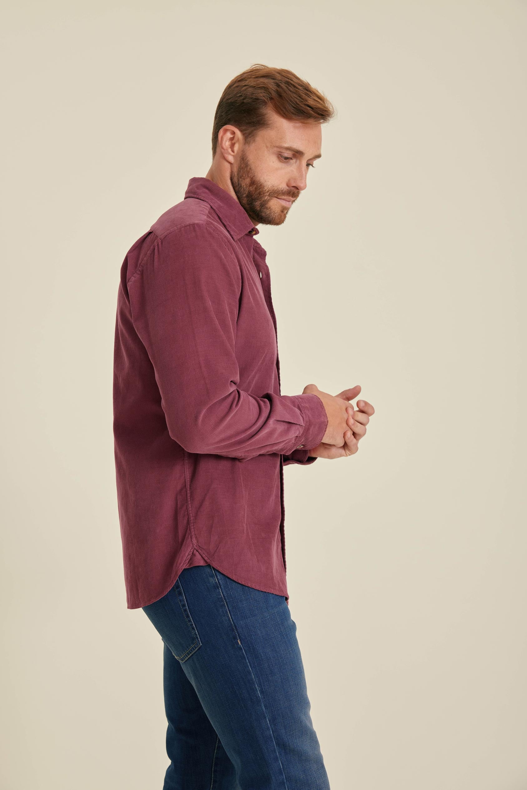 Man wearing a maroon shirt and blue jeans against a beige background