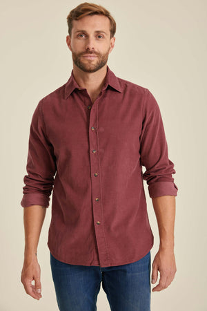 Man wearing a burgundy button-up shirt and blue jeans against a beige background