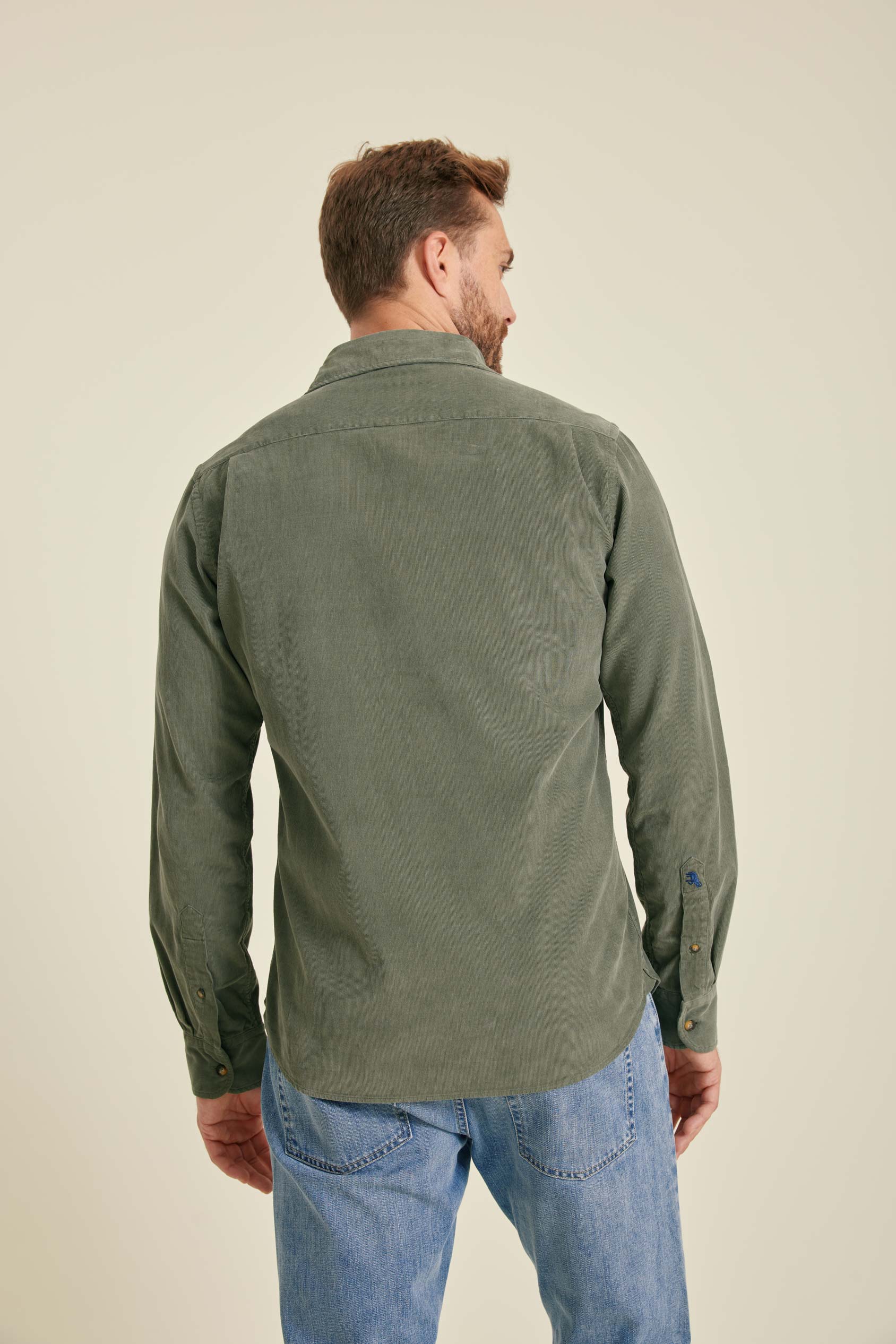 Man wearing a green shirt and blue jeans on a beige background