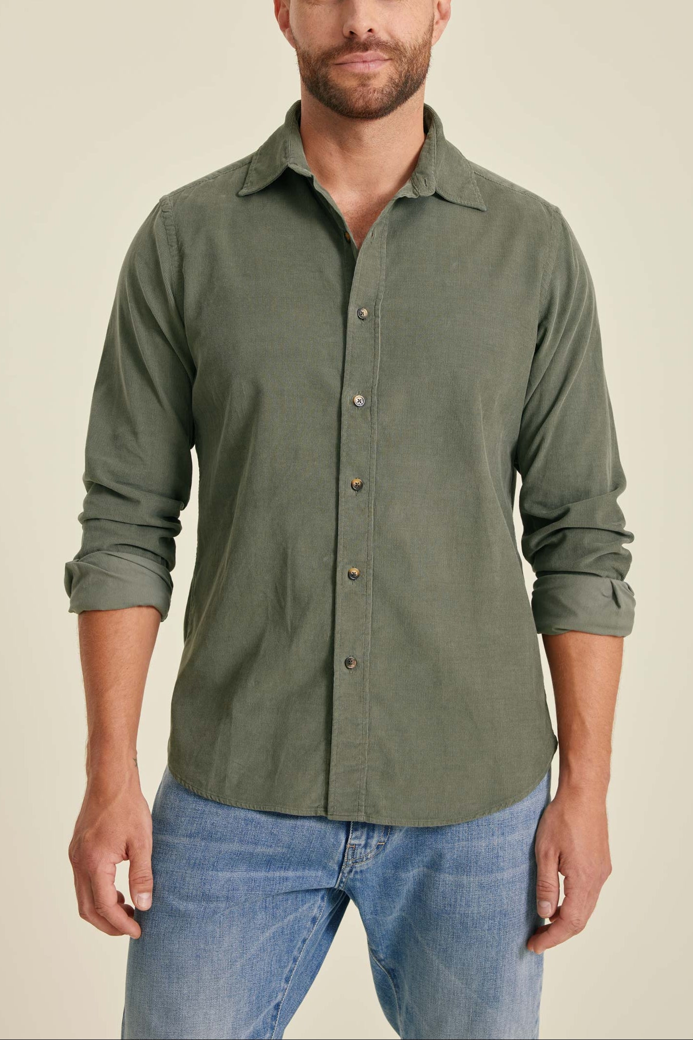 Man wearing a green button-up shirt and blue jeans against a beige background