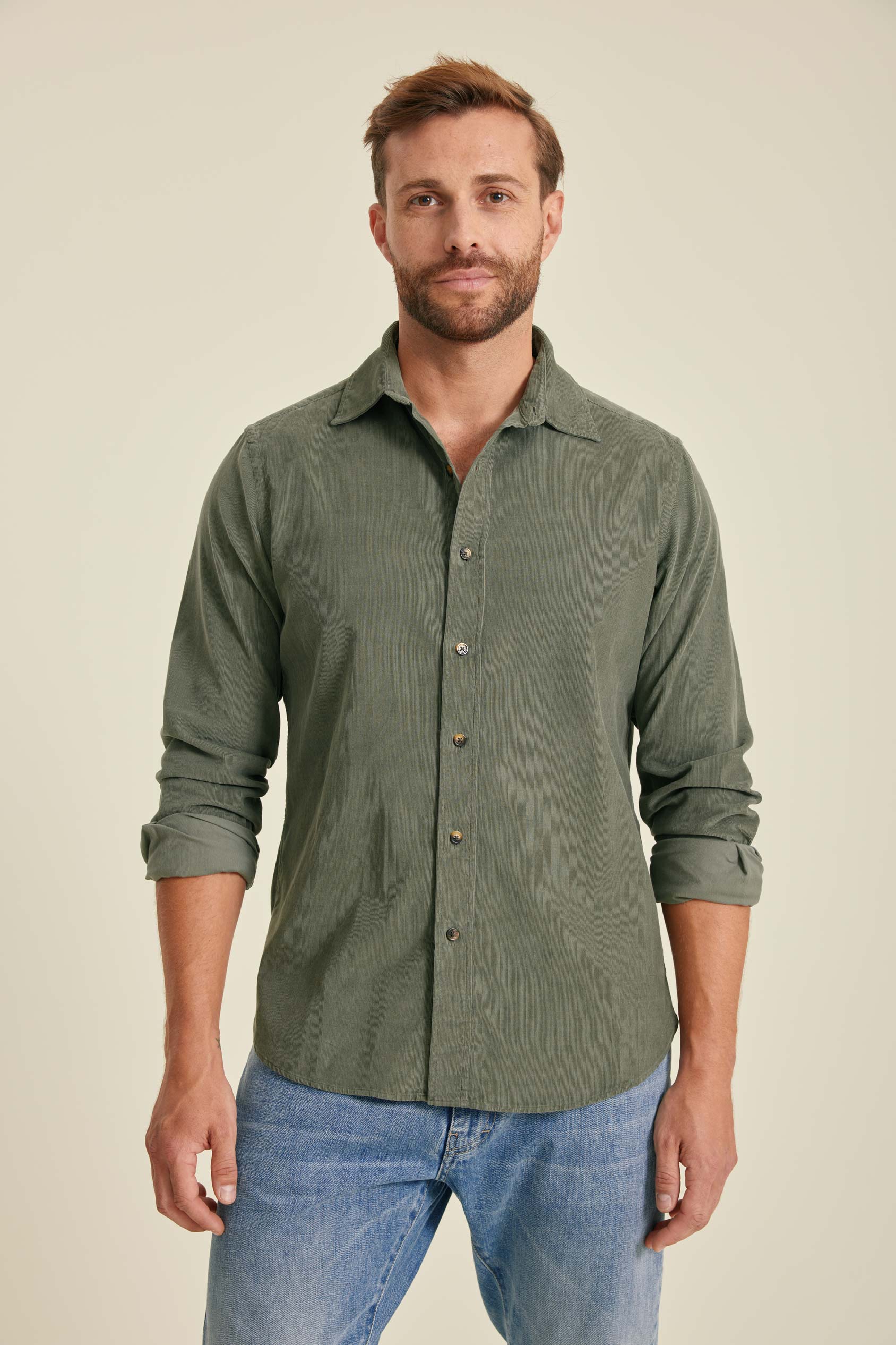 Man wearing a green button-up shirt and blue jeans against a beige background
