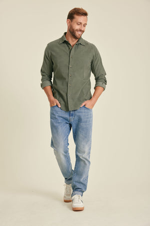 Man wearing a green shirt and blue jeans on a beige background