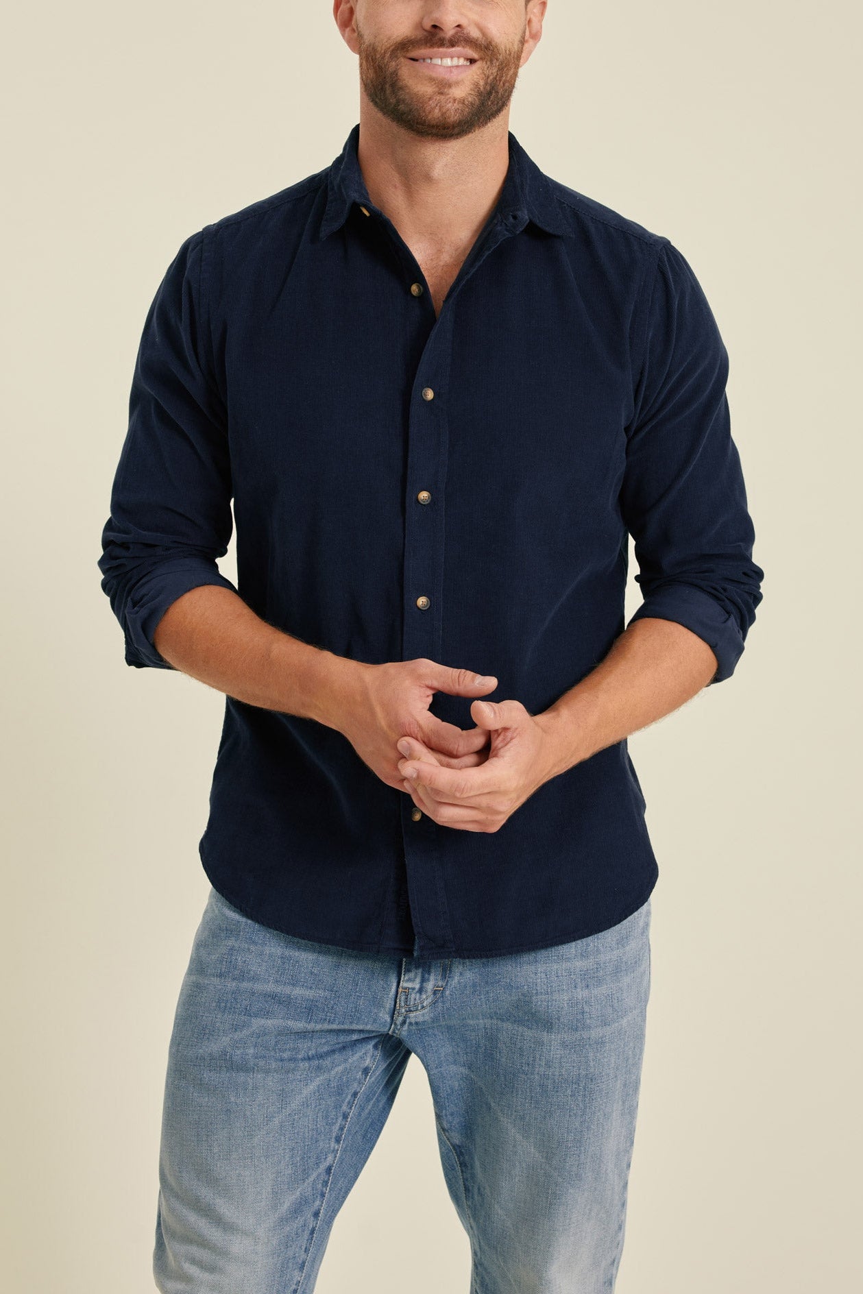 Man wearing a navy button-up shirt and light blue jeans against a beige background