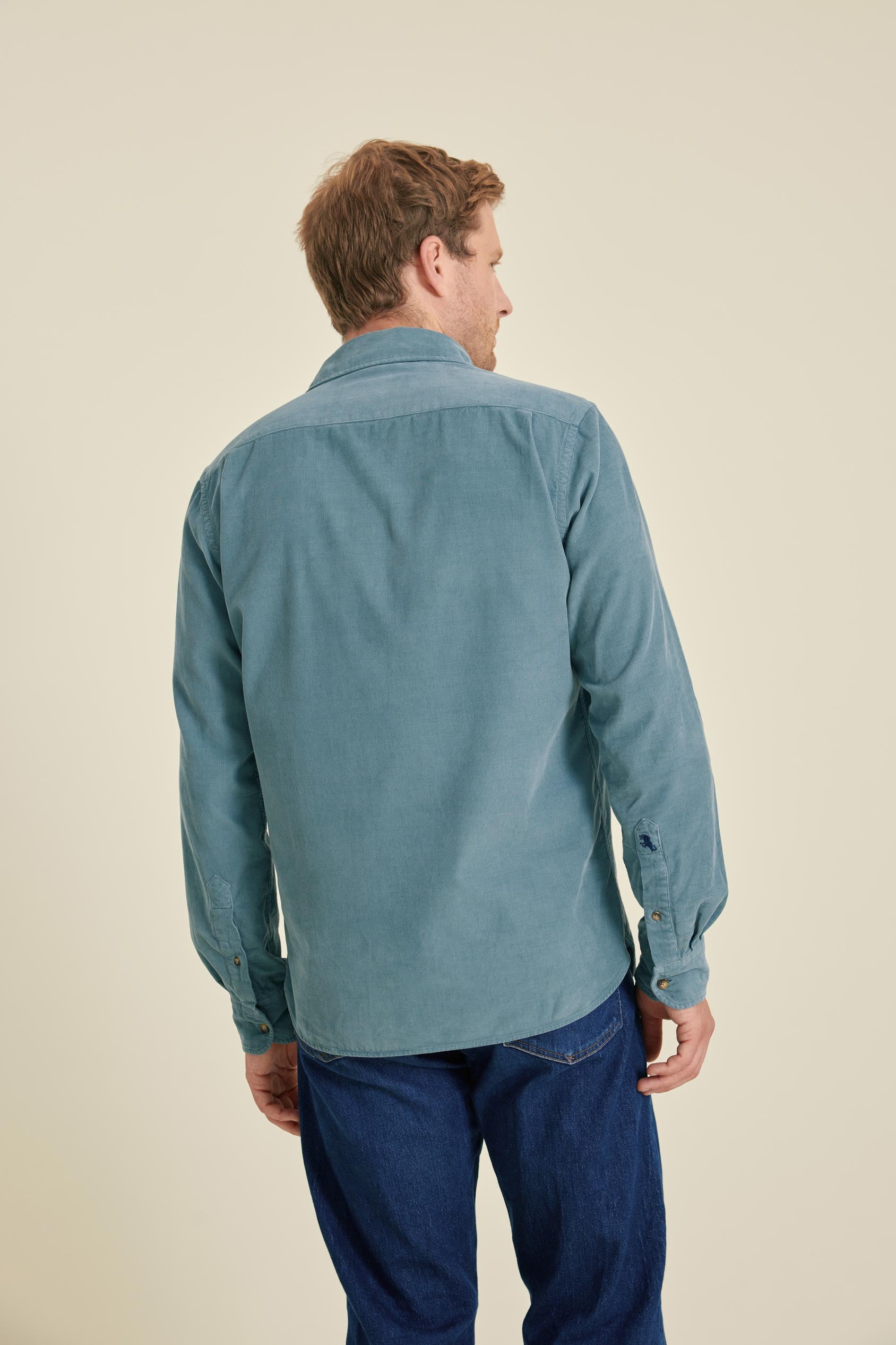 Man wearing a teal shirt and blue pants on a beige background