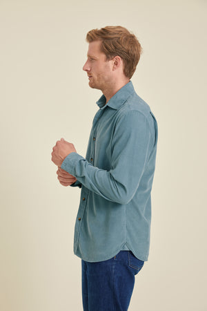 Man wearing a light blue shirt and blue pants against a beige background