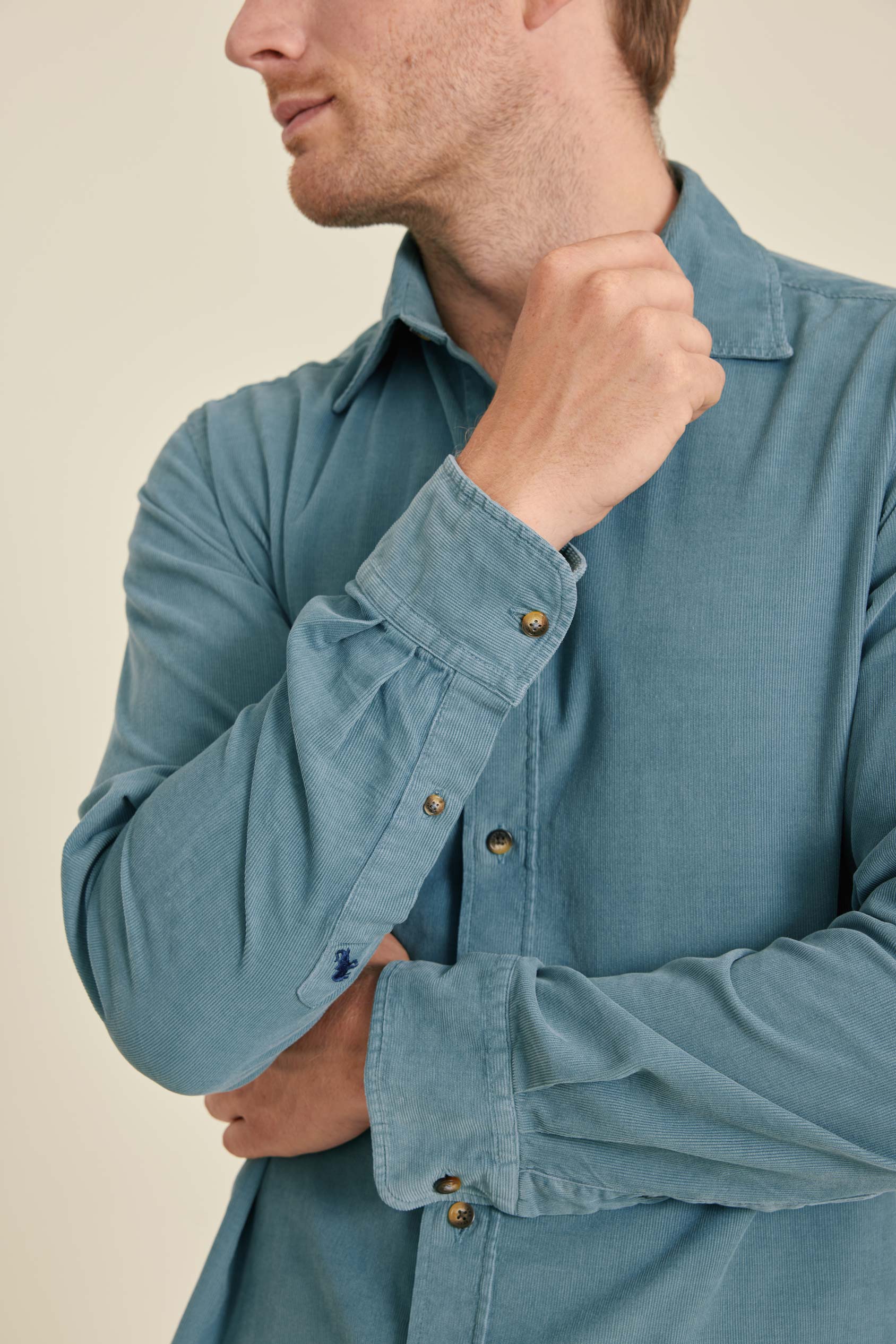 Man wearing a blue denim shirt with rolled-up sleeves on a beige background