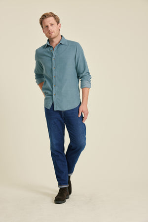Man wearing a blue shirt and jeans on a beige background